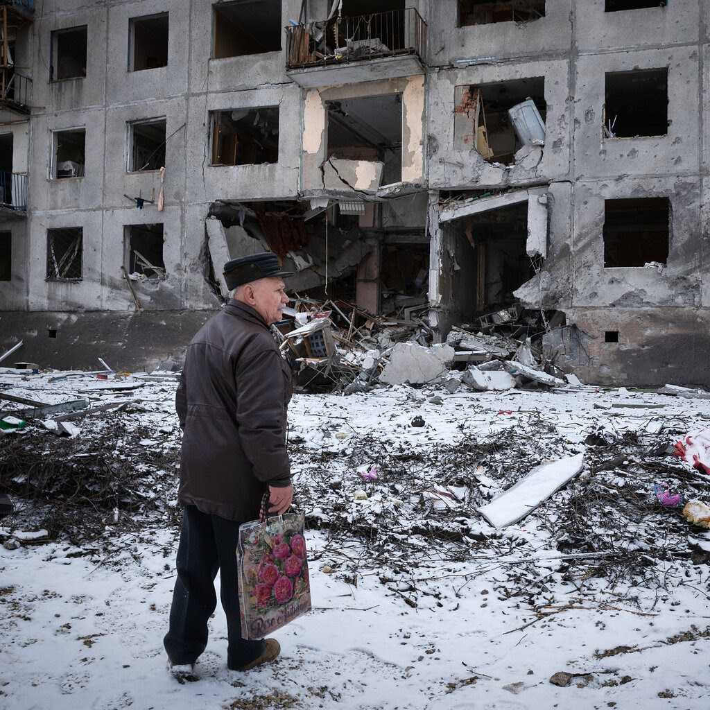 A man surveys bomb damage, standing amid debris outside a partially gutted building.