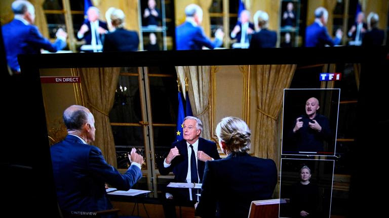 TOPSHOT - France's Prime Minister Michel Barnier (C) is seen on monitors as he delivers remarks during a televised interview by news anchors Gilles Bouleau (L) and Anne-Sophie Lapix (R), broadcasted on the evening news on French TV channels TF1 and France 2, at Hotel Matignon in Paris, on December 3, 2024. France is headed into a new political crisis on December 3, 2024, as opposition lawmakers vowed to topple the minority government of Prime Minister Michel Barnier in a no-confidence vote after just three months in office. A standoff over an austerity budget follows months of tension since President Emmanuel Macron appointed the 73-year-old in September. (Photo by JULIEN DE ROSA / AFP)