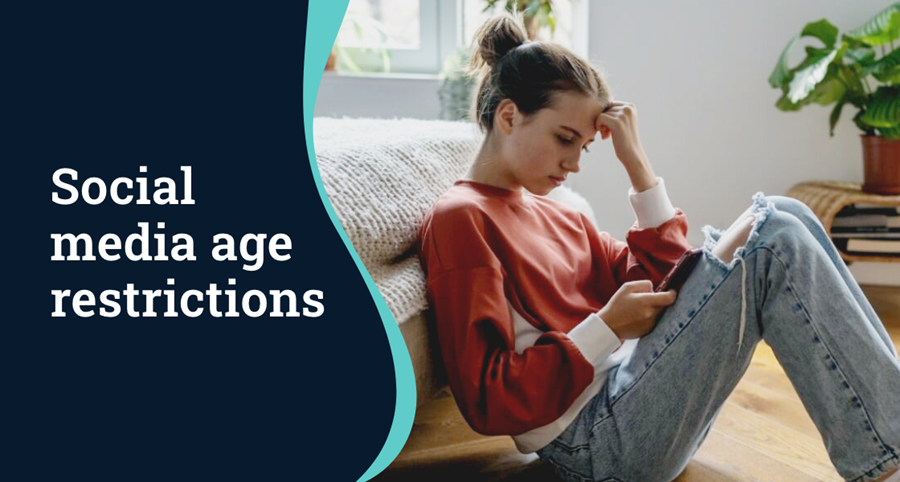 A teenager sits against a bed looking at her phone. Text on left hand side reads: 'Social media age restrictions'