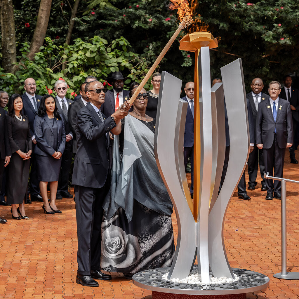 Paul Kagame and his wife lighting a flame atop a sculpture with a long torch.