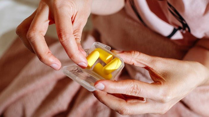 A person holds a box of yellow earplugs. You may be more prone to have earwax buildup if you wear earplugs and earbuds regularly.