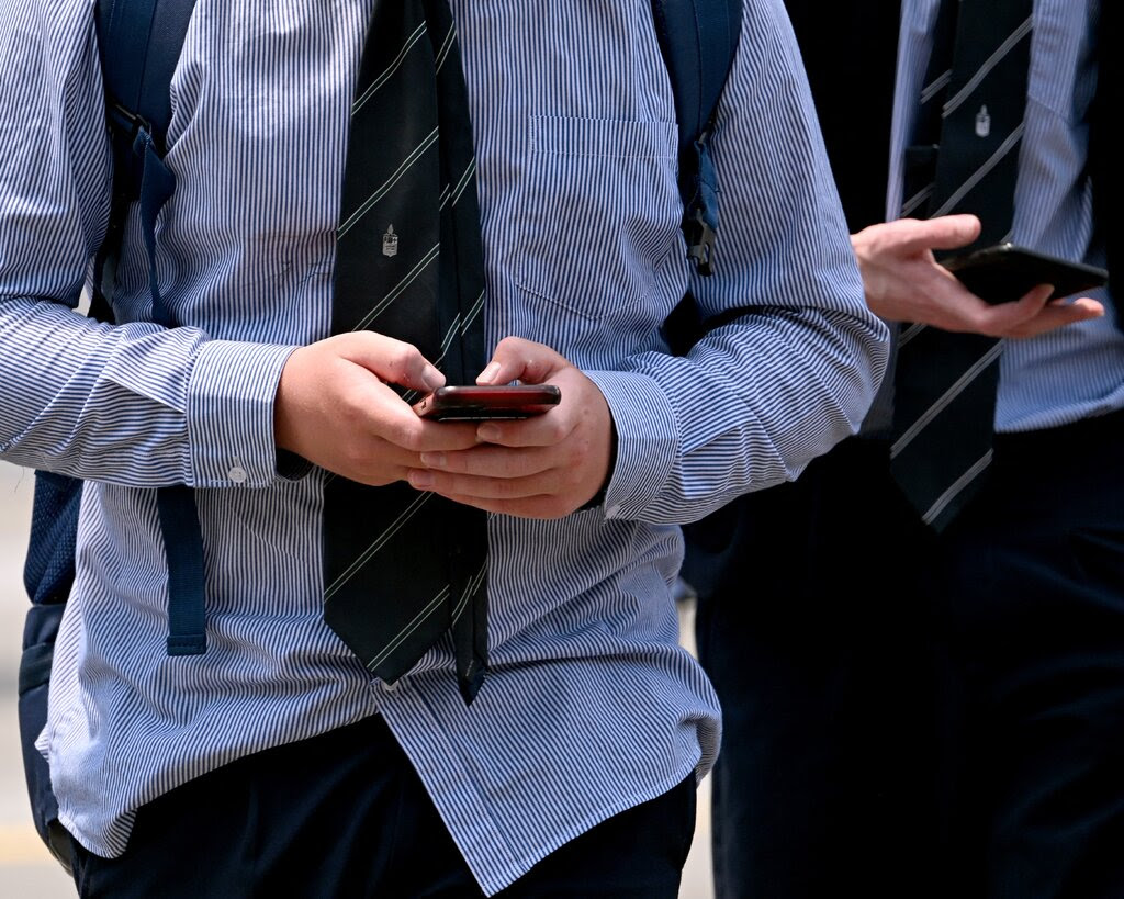 Two boys wearing school uniforms looking at their phones.