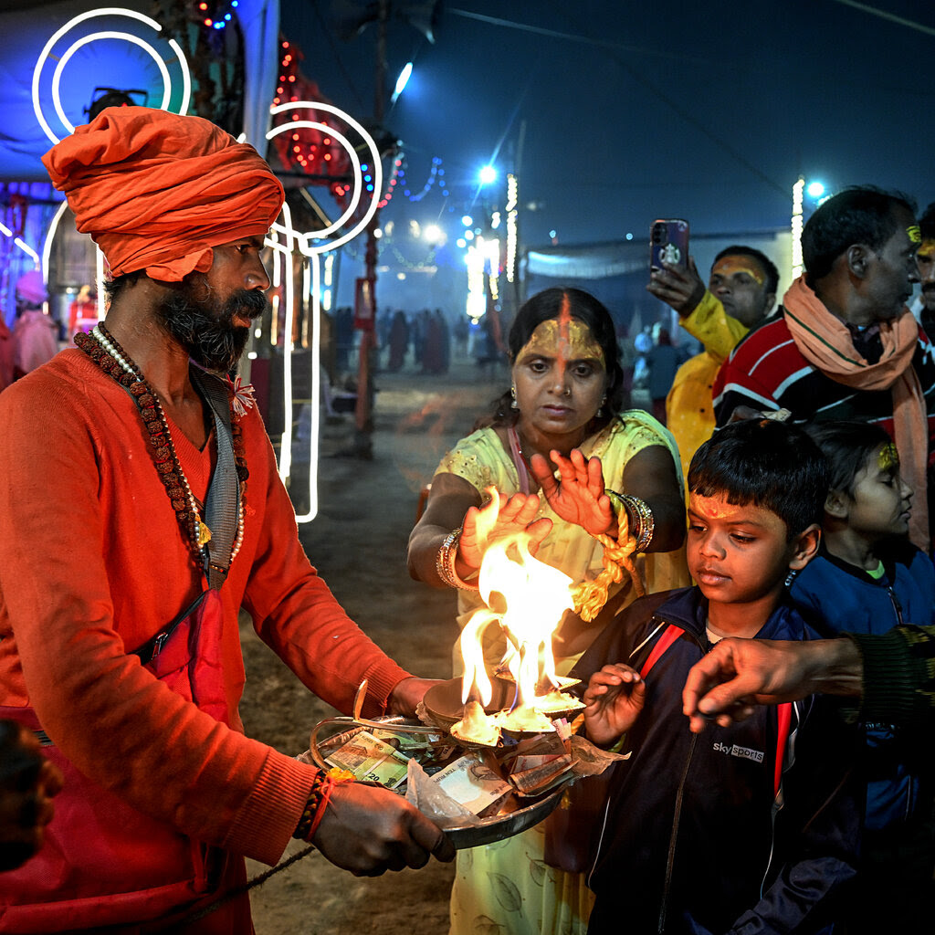 People praying near a saffron-dressed man with a tray that bears a ritual flame and cash donations.