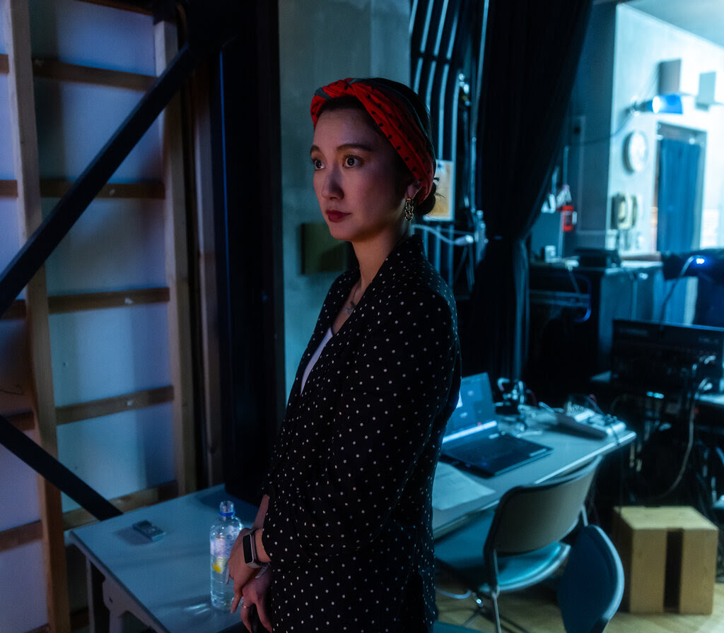 Shiori Ito stands in shadow next to a desk with a laptop.