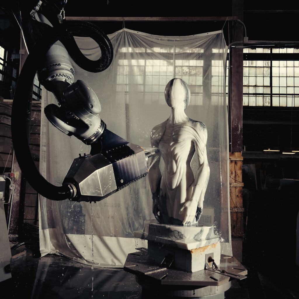 A robot arm carving a humanoid torso.