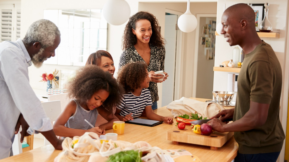 A Black family gathers together in a kitchen to talk.