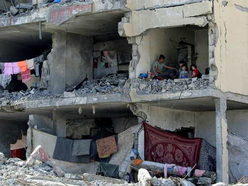 Un Palestinien et ses enfants sont assis mercredi dans une pièce détruite d'un immeuble résidentiel à Rafah, dans le sud de Gaza.