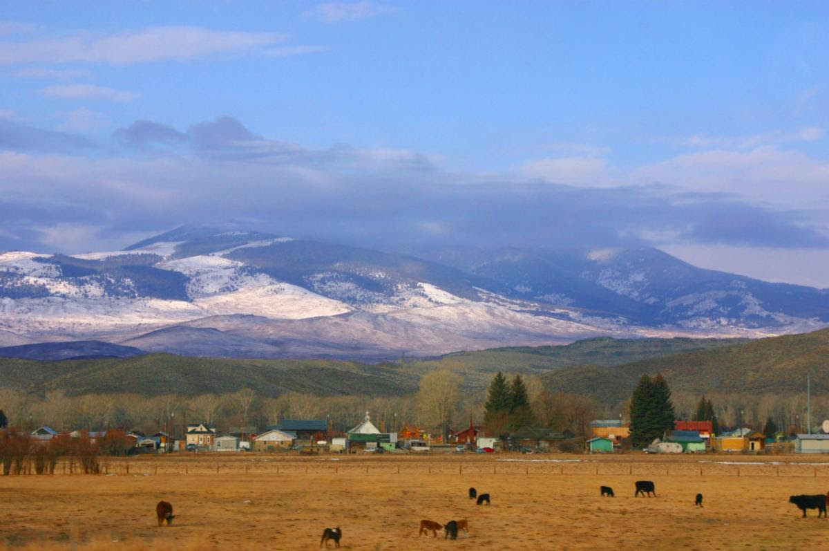 Landscape with snow-capped mountains in the background and a field and a small town in the foreground.