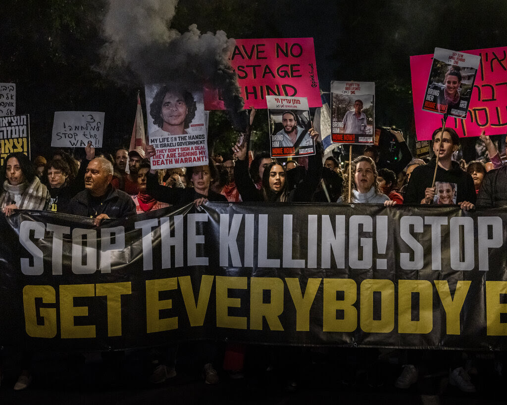 Protesters hold up placards and a banner, partially reading “Stop the Killing!”