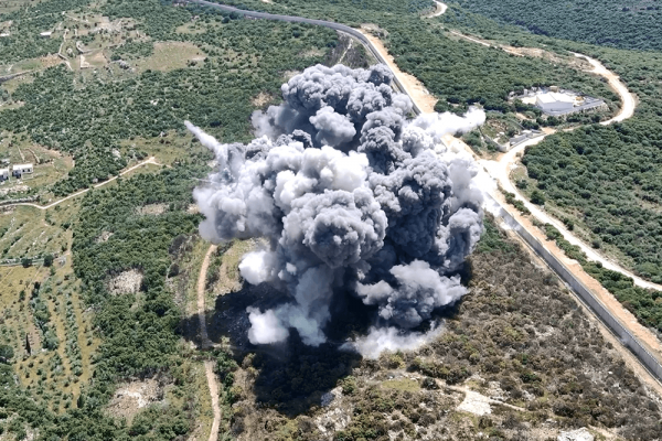 Drone explodes and releases cloud of gray snoke over rural green and brown area with a road and river to the right. 