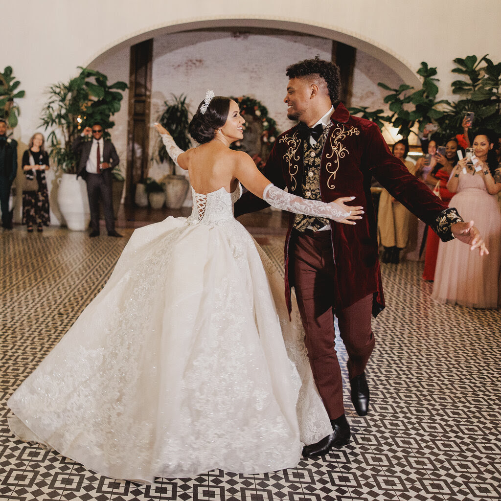 Philicia Saunders, in a white dress, dances with Jordan Wilson, who is wearing a burgundy tuxedo, with a Regency-style coat. 