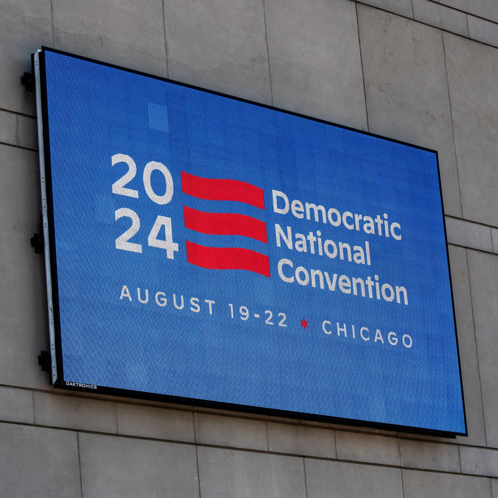 A screen reads “2024 Democratic National Convention, August 19-22, Chicago.”