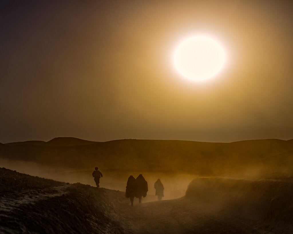 A hazy sun shines overhead as people walk through dusty terrain. 