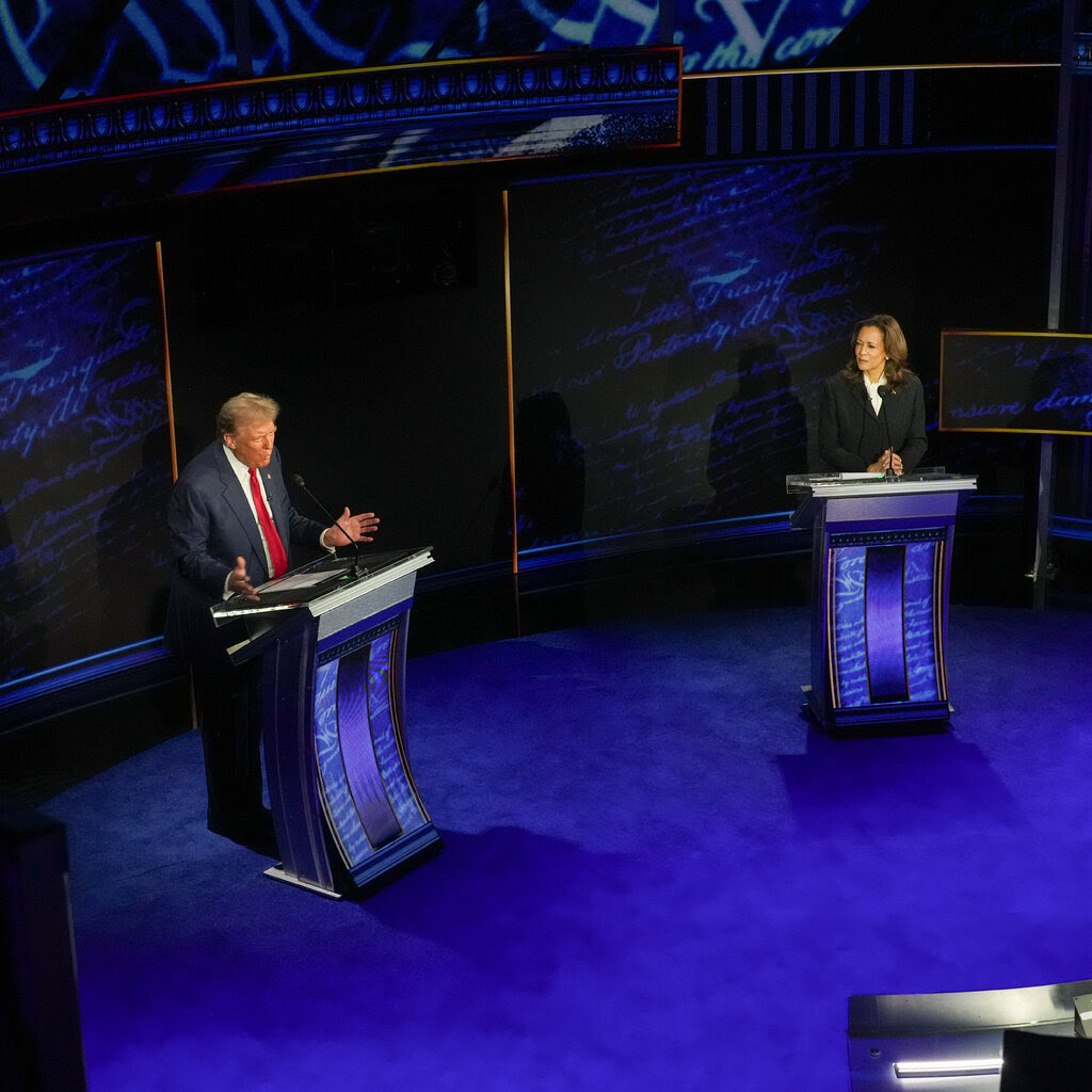 Vice President Kamala Harris and former President Donald J. Trump stand on a debate state. They are each at a lectern. Mr. Trump has his arms open, while Ms. Harris looks at him.