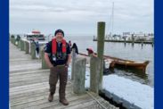 Roy Arezzo stands on a dock wearing a life jacket next to several boats.