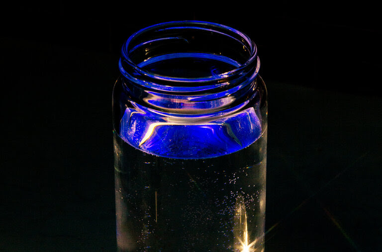 A glass bottle containing hydrogen water in a darkly lit room.