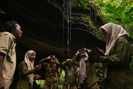 A man dressed in ranger’s uniform with a group of women in headscarves, with binoculars, stand in a rainforest