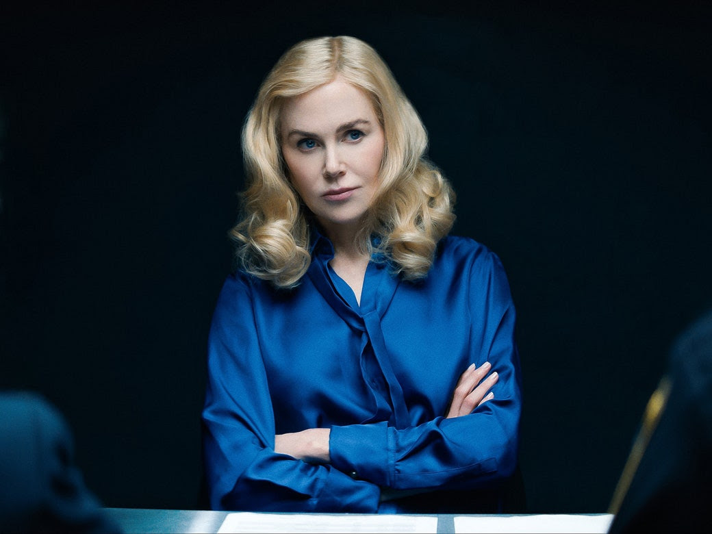 A blonde woman in a blue shirt sitting with her arms crossed.