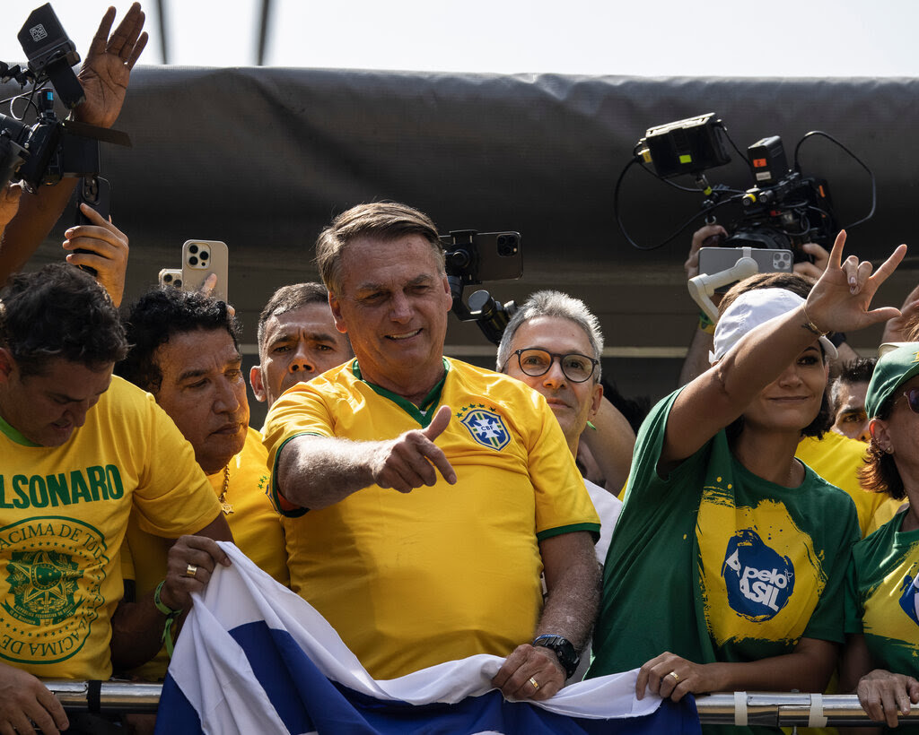 Jair Bolsonaro standing in the middle of a group of supporters and waving to the crowd below.