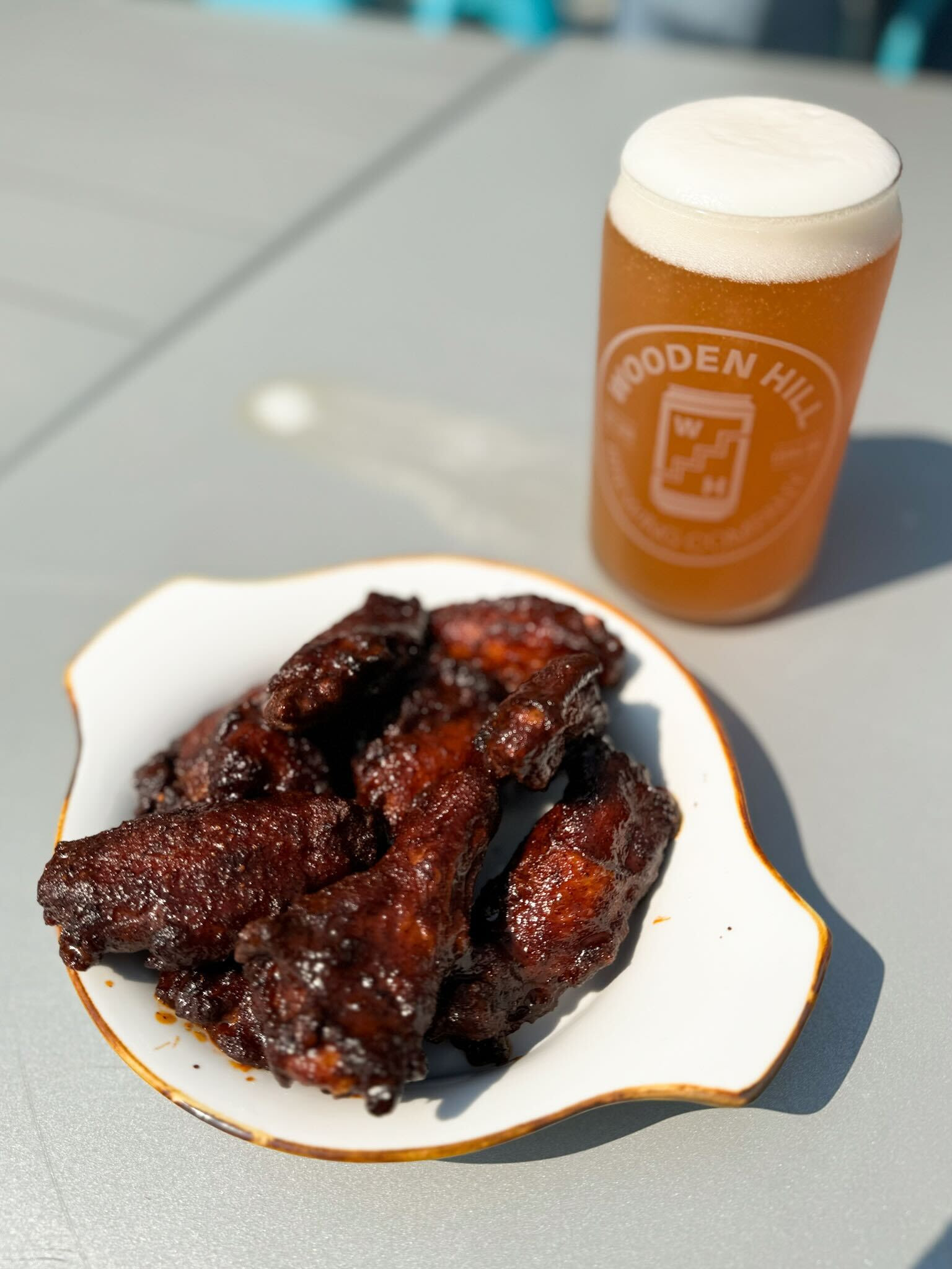 image of a white dish full of chicken wings with a full pint of light beer in the background.