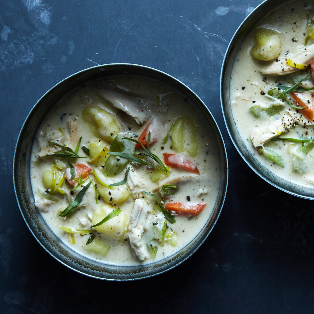 Chicken soup with gnocchi dumplings, displayed in metal bowls on a dark table.