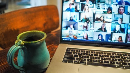 Computer with an online meeting, coffee cup next to it on table