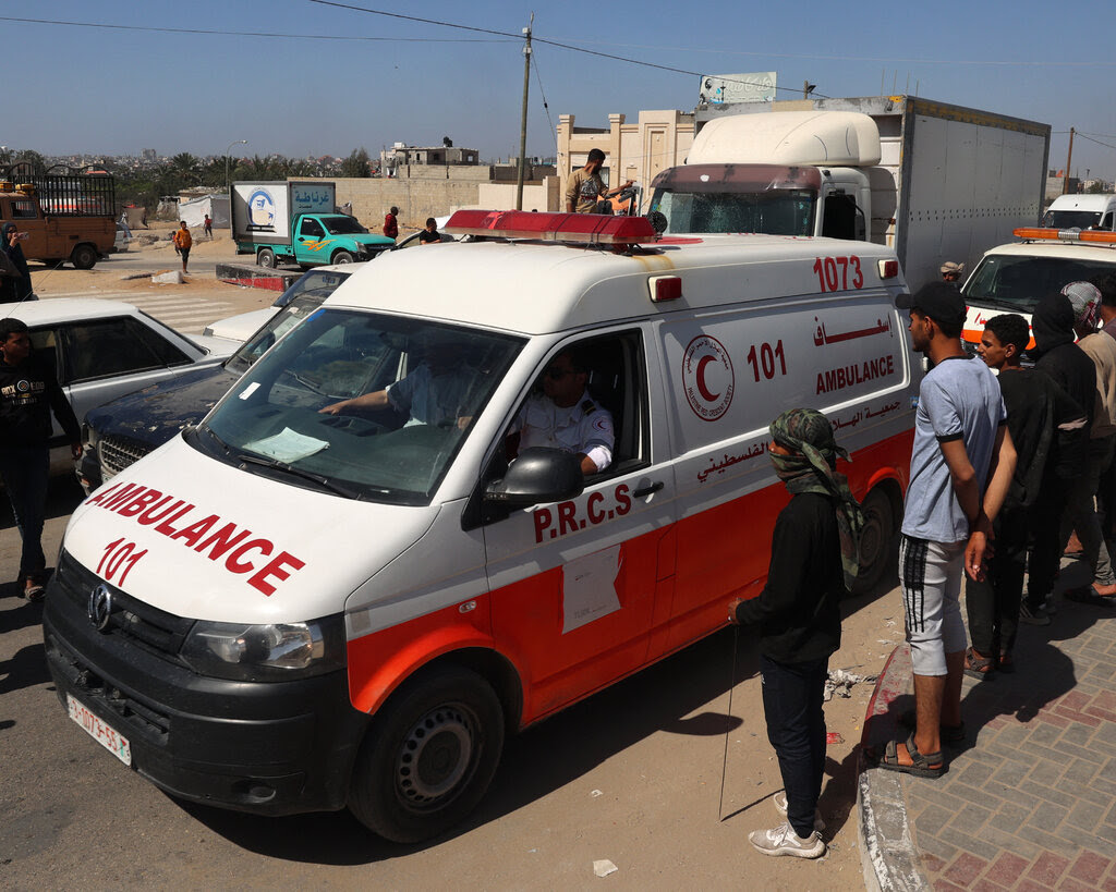 Several people watch a red and white ambulance sitting in traffic.