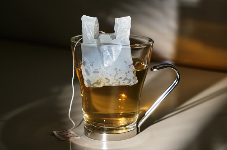 A tea bag in the shape of a plastic bag floats in a clear cup of tea.