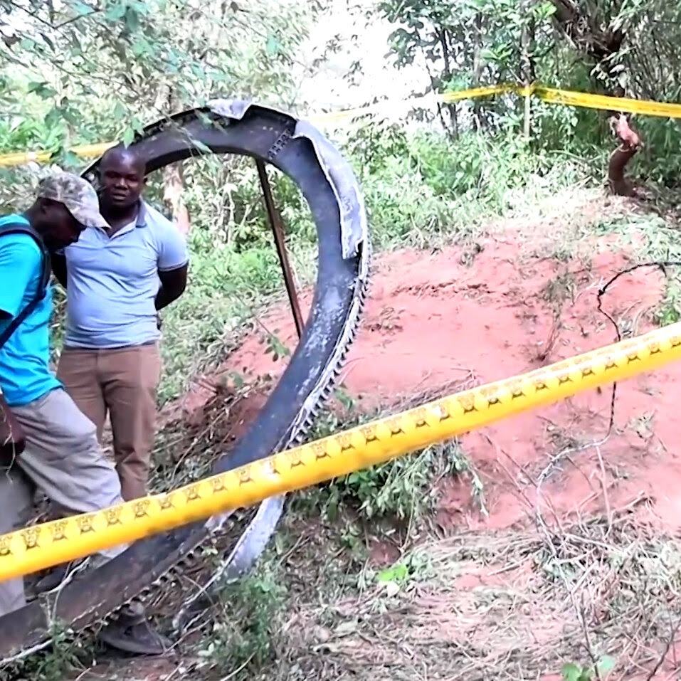 Two men standing near a metal ring in an area cordoned off by yellow tape. 