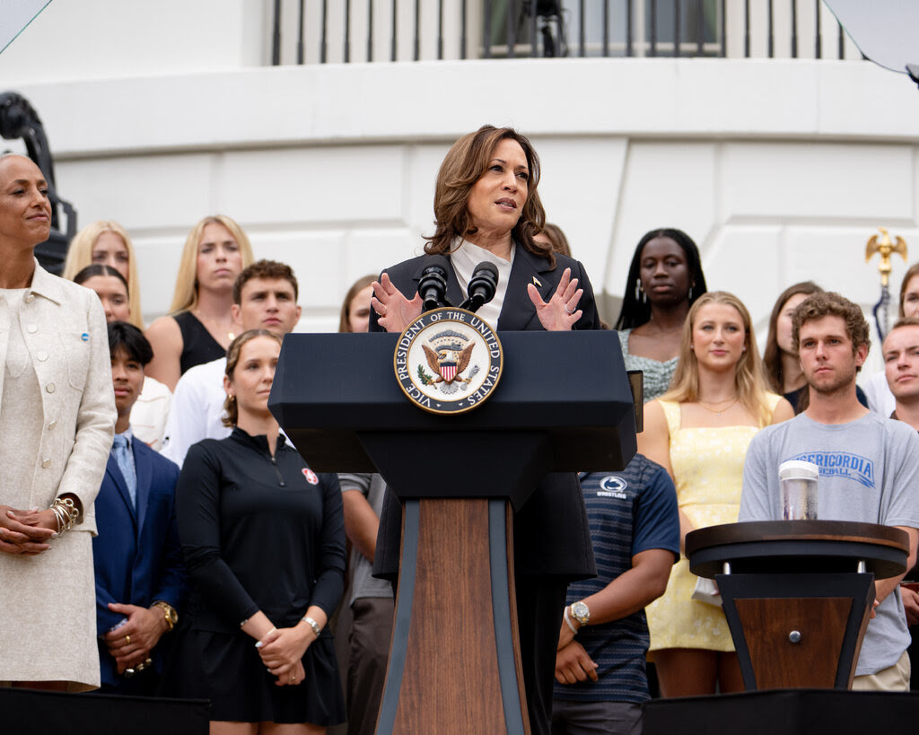 Kamala Harris speaking at a podium surrounded by people.