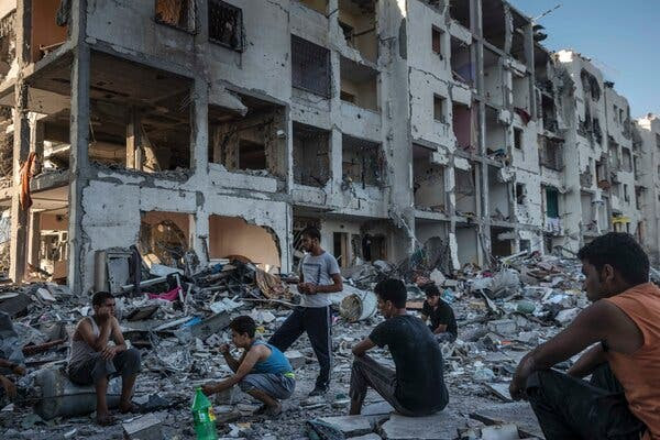 A handful of people gather outside a large residential building that was destroyed by airstrikes.