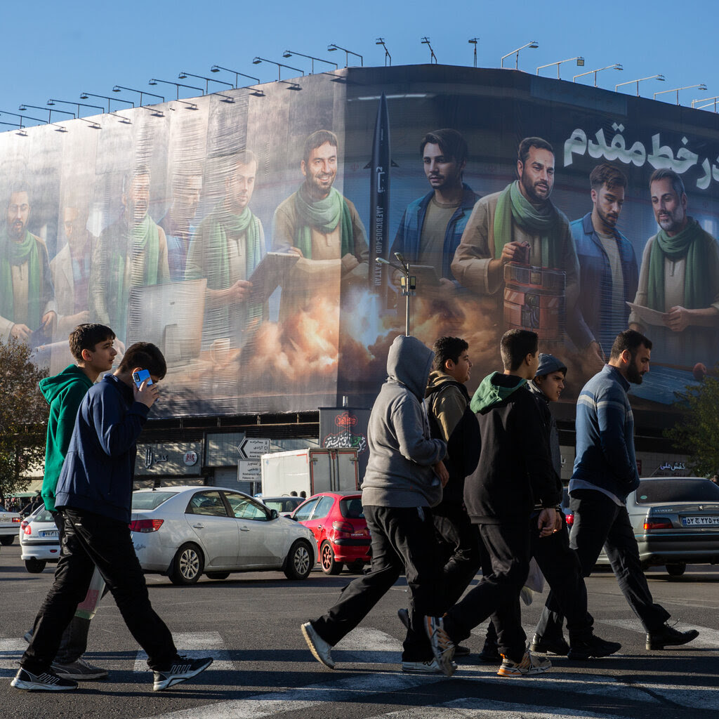 A group of people cross a street in front of a mural in Tehran, Iran.