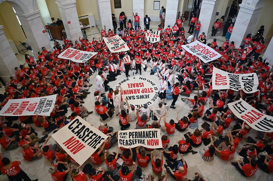 An overhead photo of demonstrators protesting in the rotunda of the Capitol. They are wearing red shirts and there are banners with slogans such as "Ceasefire now" and "Let Gaza live."