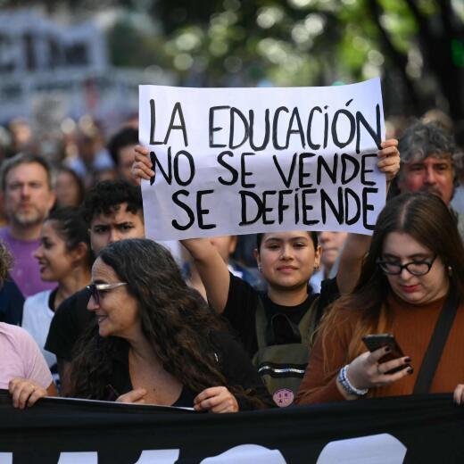 A demonstrator (R) holds a sign that reads "Education is not for sale, it is defended" during a march in protest of the budget adjustment to public universities in Buenos Aires on April 23, 2024. Thousands of university students took to the streets of Argentina on Tuesday to repudiate the defunding of the public university, which was declared in a state of budgetary emergency in the framework of the adjustment policy of the right-wing president Javier Milei. (Photo by Luis ROBAYO / AFP)