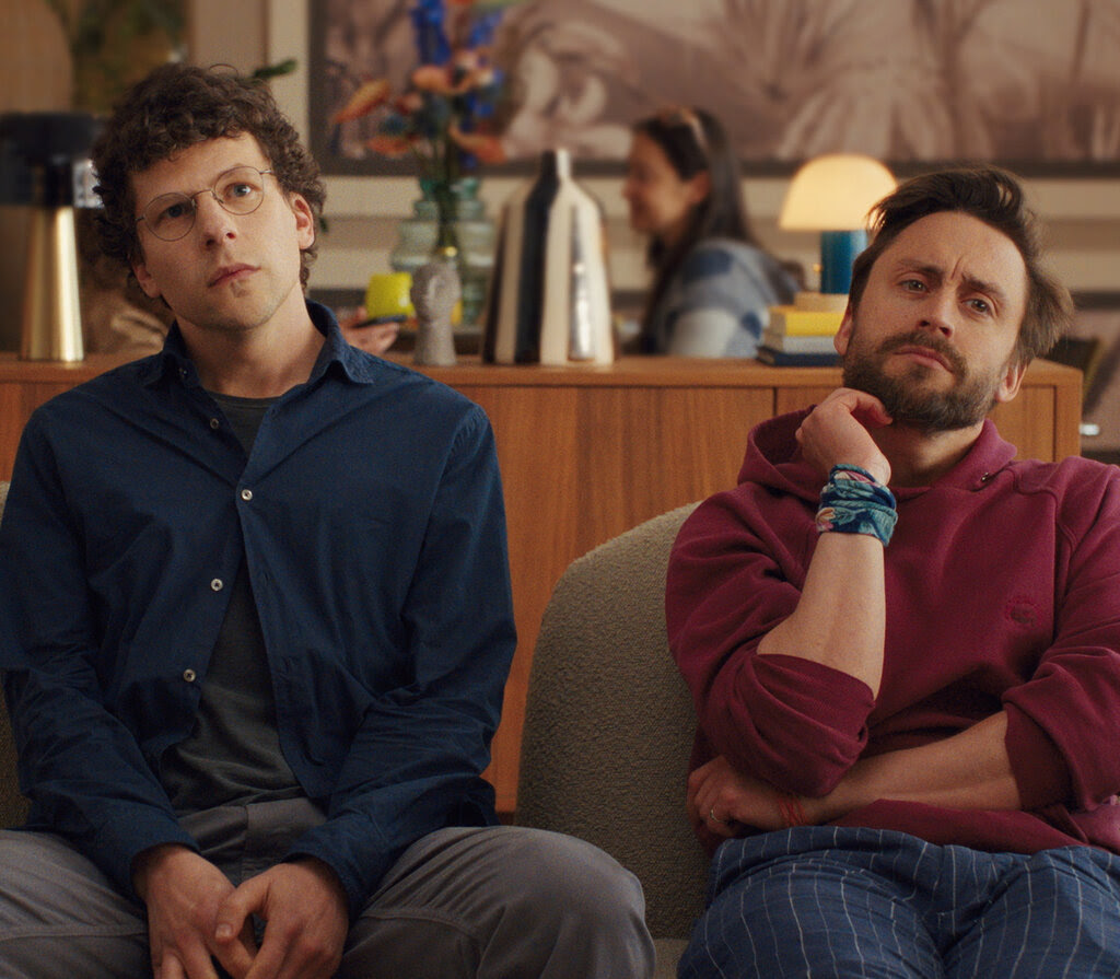 Two men, seated on chairs in a lobby-type area, looking thoughtful. 