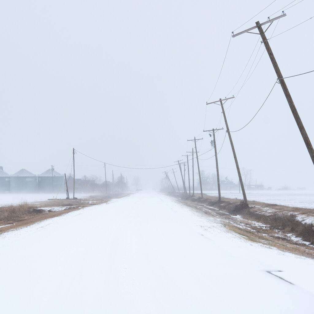 A snow-covered road lined by leaning power lines.