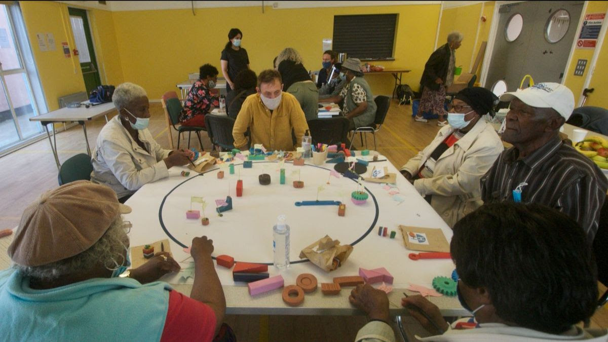 five people are sitting around a table that is covered in a large circle on which there are placed blocks and other small toy-like objects 
