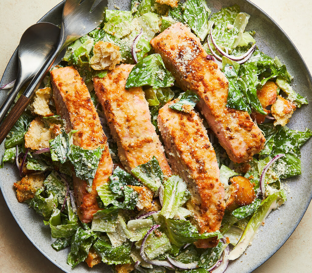 Parmesan-crusted salmon Caesar salad on a gray plate with a serving fork and spoon.