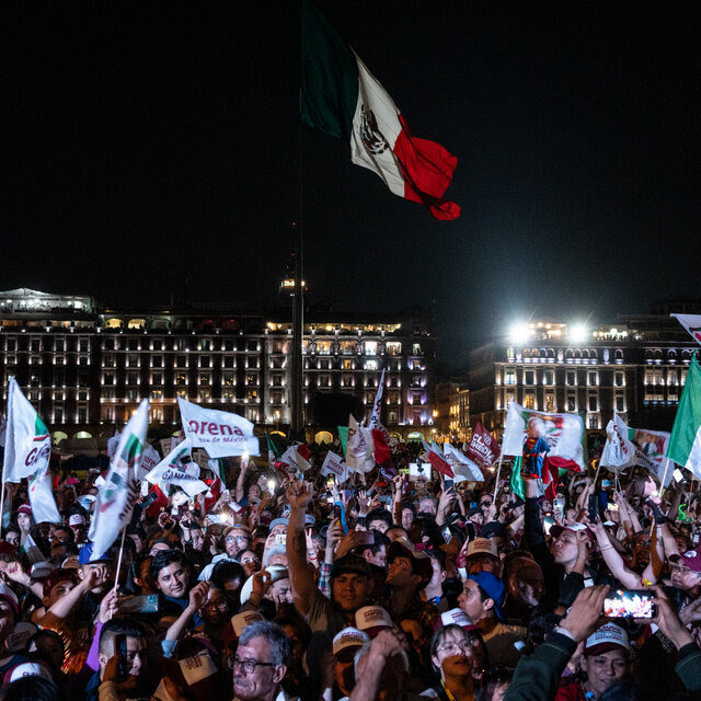 A crowd of people outside at night. Many of them are waving flags. 