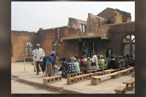 Church members are seated on cinder blocks in a burned out church.