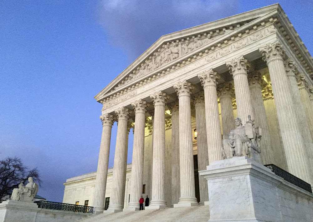 The front facade of the Supreme Court building is show against a blue sky.