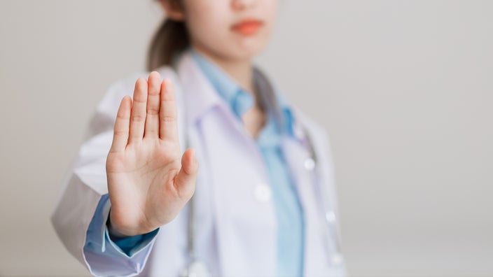 A healthcare professional holds up their hand in a stop gesture.