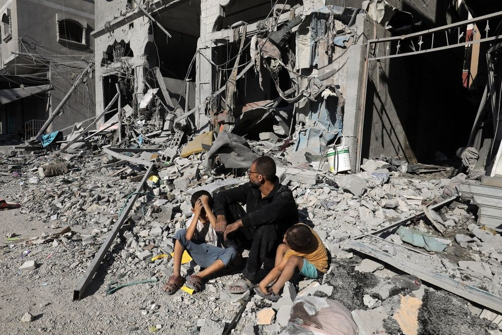 Un Palestinien et deux enfants assis au milieu des décombres d'une maison détruite par une frappe aérienne israélienne dans la ville de Rafah.