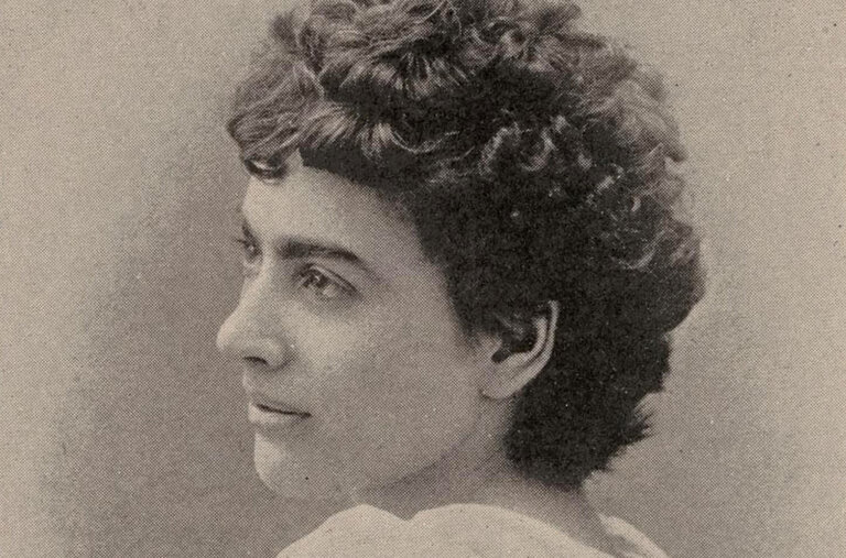 A black and white portrait of Lizzie Magie in profile, a woman with short curly hair and sharp facial features.