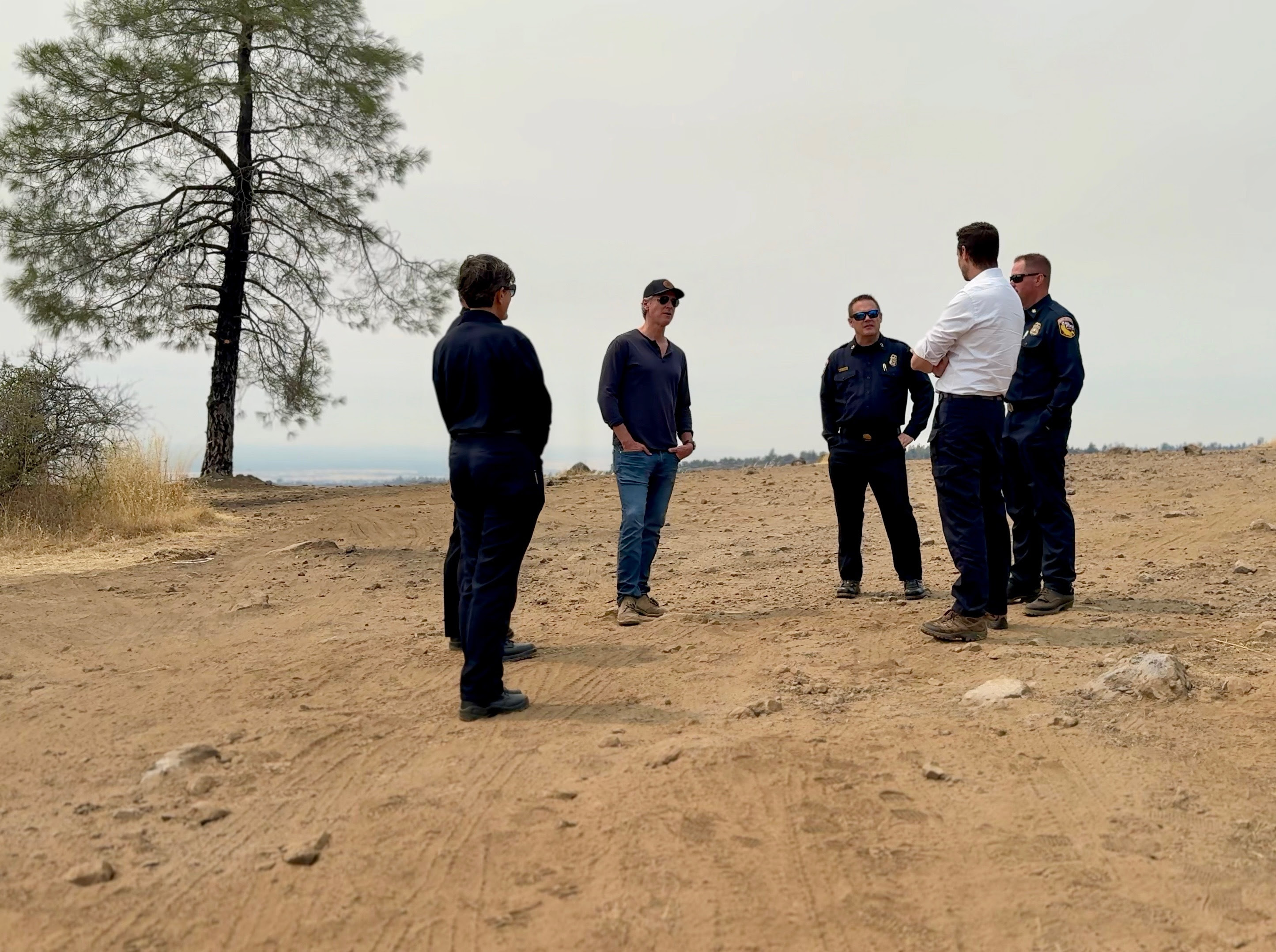 Governor Newsom standing on a dirt road and speaking with a group of firefighters