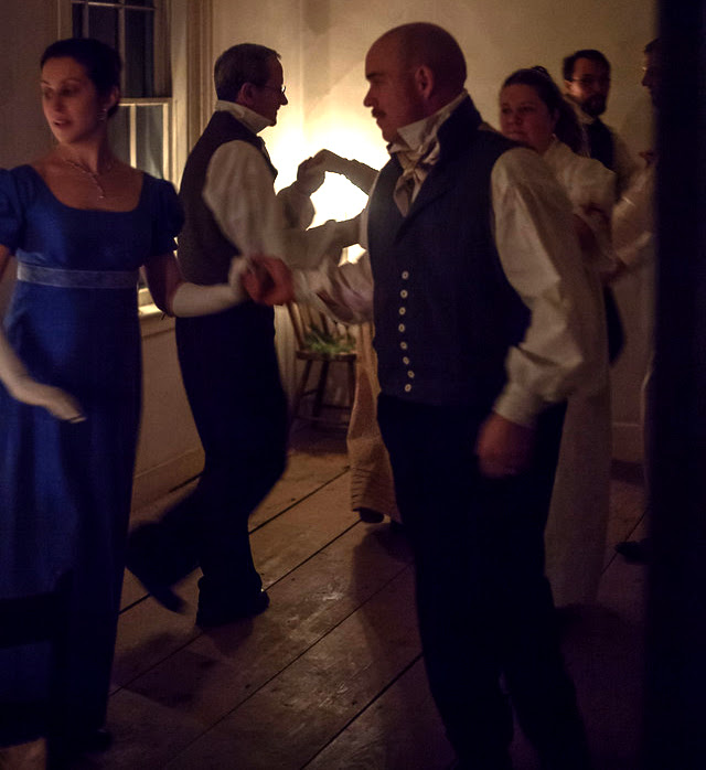 People dressed in historical 19th century costume dance by candlelight