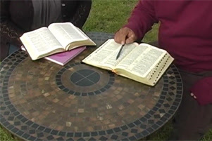 Two people are studying Bibles while sitting at a mosaic style tabletop. No faces can be seen.
