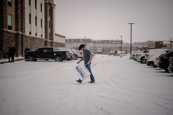 A man in short-sleeve shirt and a black cowboy hat walks across a snow-covered street. He is carrying a sign reading “Truth Vivek.”