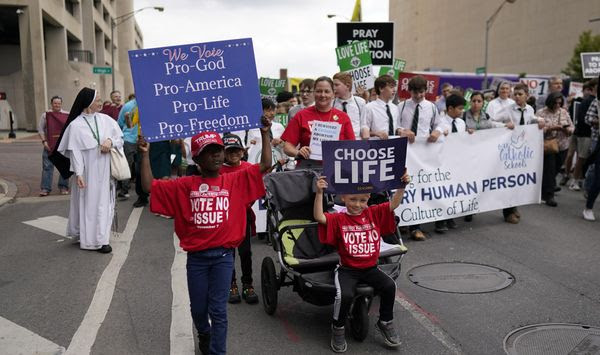 From left, Gianna Young, holding a sign that reads &quot;We Vote Pro-God Pro-America Pro-Life Pro-Freedom&quot; and her brothers Lucas and Isaac, holding a &quot;Choose Life&quot; sign, march with their mom, Erin Young, during the Ohio March for Life in Columbus, Ohio, Friday, Oct. 6, 2023. All three children are adopted. (AP Photo/Carolyn Kaster) ** FILE **