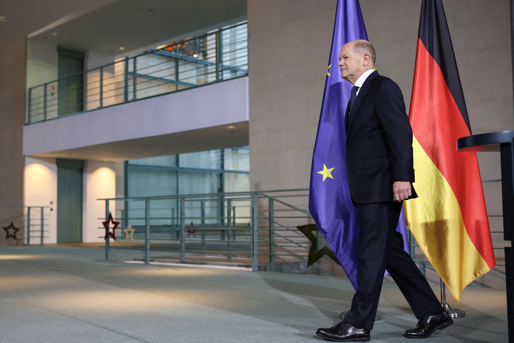 Olaf Scholz walking near a German flag and a European Union flag.